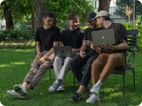 Bench group picture about team holding 2 MacBooks: Four of the Once Advertisements employees, Kristof Menesi, Krisztian Mezei, Matyas Laneury, and Gergo Mezes sitting on a bench in the ‘Museum Garden’ in Hungary.