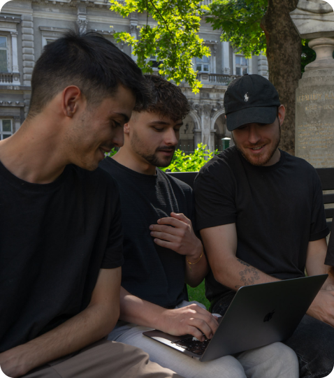 Bench group picture about team holding 1 MacBook: Three of the Once Advertisements employees, Krisztian Mezei, Matyas Laneury, and Gergo Mezes sitting on a bench in the ‘Museum Garden’ in Hungary.